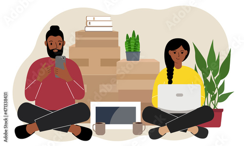 Couple sitting cross-legged with mobile phone and laptop, ordering delivery. Lots of things in cardboard boxes. The family is preparing to move to another house.