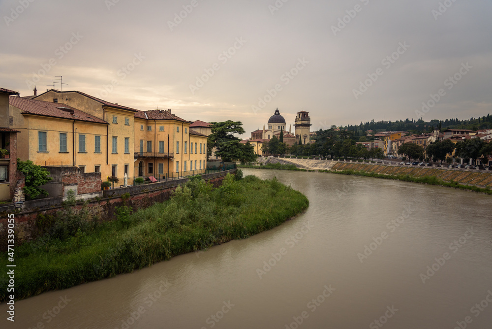 Colorful facades of the old town buildings by the Adige river with the parish of San Giorgio in Braida in the background on a cloudy day, Verona, Veneto Region, Italy