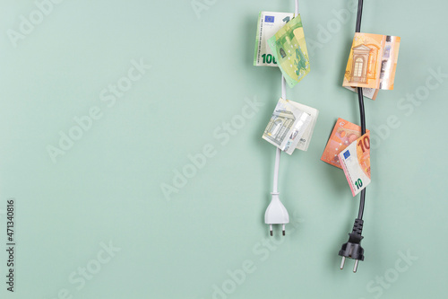 Foto Electric power plugs with Euro banknotes on them hanging on light green background
