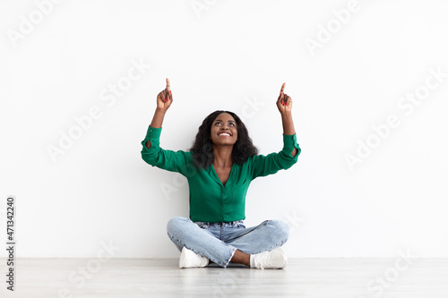 Cheerful young black woman sitting on floor, showing copy space