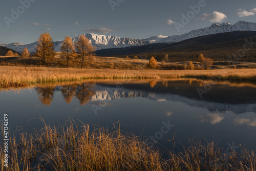 A serene view of the mountain range reflected in the lake. The mountain peaks are covered with snow. Clear sunny autumn day. Altai. Lake Dzhangyskol. The nature of Siberia.