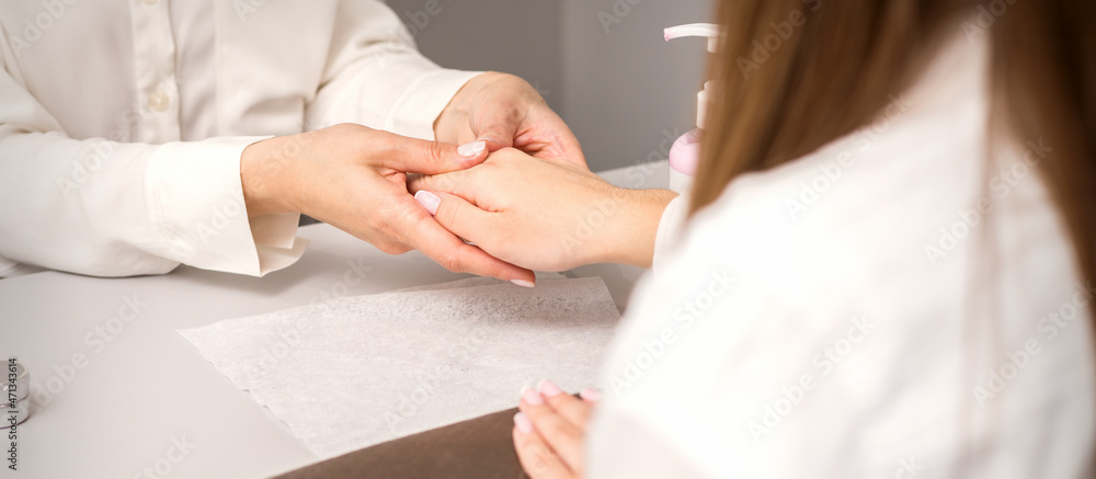 Manicure master massaging female hands before nail procedure in a nail salon Manicure master massaging female hands before nail procedure in a nail salon