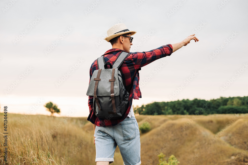 man with a backpack on a country walk on a summer day. Young people hiking in the countryside, outdoors at sunset