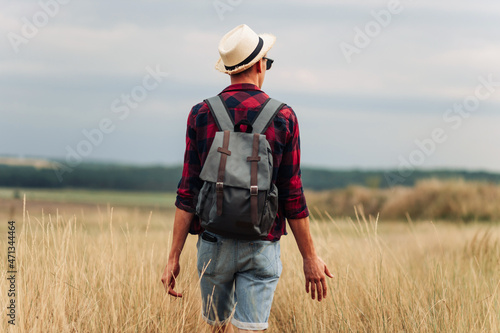traveler with a backpack, walks in a field at sunset. Male tourist walks and enjoys the view of the beautiful nature © Shopping King Louie