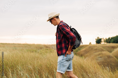 traveler with a backpack, walks in a field at sunset. Male tourist walks and enjoys the view of the beautiful nature © Shopping King Louie