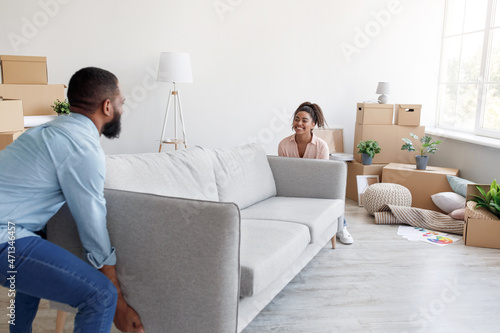 Positive millennial african american family carry sofa to new apartment with cardboard boxes