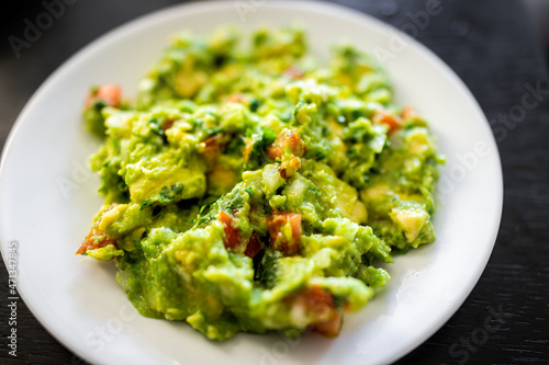 Above macro closeup view of guacamole dish on white plate made with ripe green avocado, garlic tomatoes and cilantro