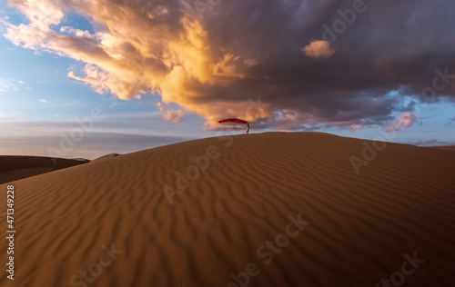 Girl walking on the sand dunes in the distance holding a red cloth