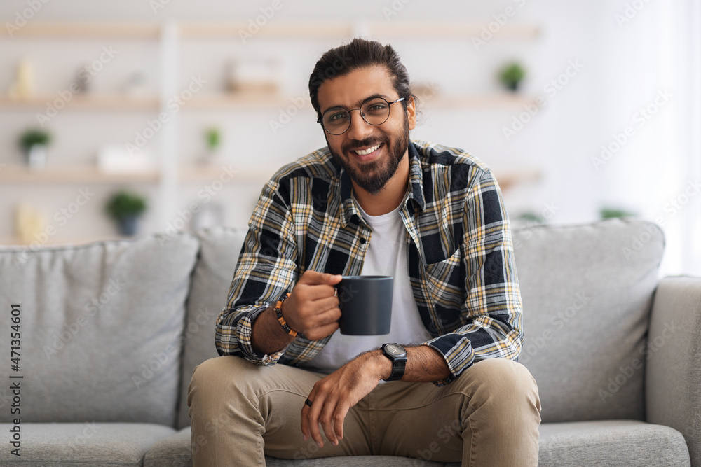 Handsome millennial arab man resting at home, drinking coffee
