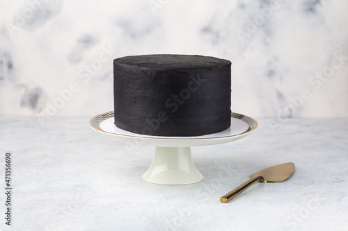 Black cake on golden cake stand, white table.