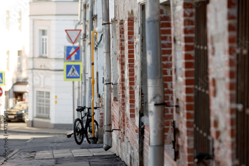 Brick wall of an old building in the historical center. Metal downpipes on the house. A street with a parked bike and road signs photo