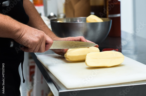 Restaurant kitchen employee cutting fresh potatoes with knife