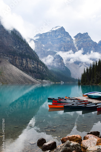 Colourful canoe lined up on turquoise blue water lake surrounded by mountains