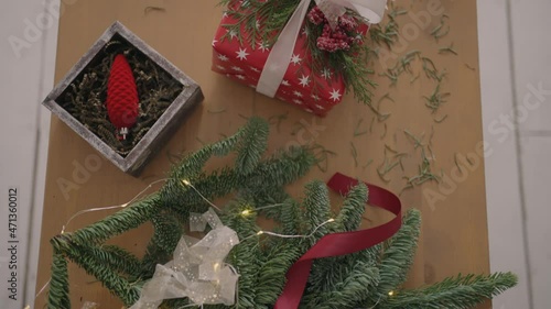 top view plan. Fully visible the table with the decorations. Female hands put and finalize Christmas gift wrapped in craftool paper on a wooden table. Bandaging tape and tied bow. photo