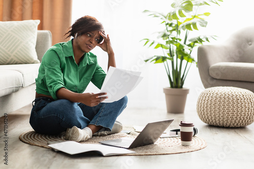 Stressed African Woman Holding Papers Sitting At Laptop At Home