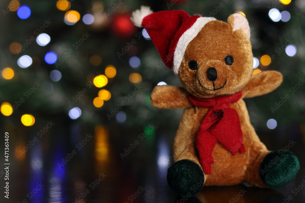 Teddy bear on a background of Christmas lights. Greeting card with place for text. Christmas tree .Holiday .Winter. Toy bear in Santa Hat and colored bokeh. Horizontal photo Teddy bear on a background of Christmas lights. Greeting card with place for text. Christmas tree .Holiday .Winter. Toy bear in Santa Hat and colored bokeh. Horizontal photo