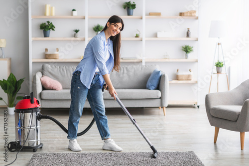 Cheerful lady cleaning rug carpet with vacuum cleaner