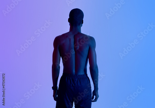 Back view of strong young black man with naked torso posing in neon light
