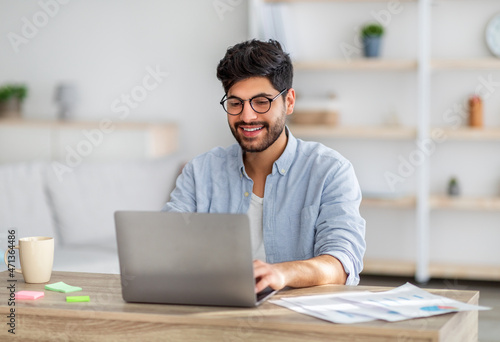 Fotografiet Portrait of happy arab freelancer man sitting at desk with laptop computer at ho