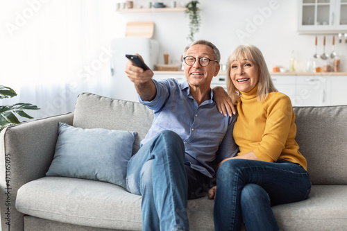 Happy Senior Spouses Watching TV Sitting And Hugging At Home