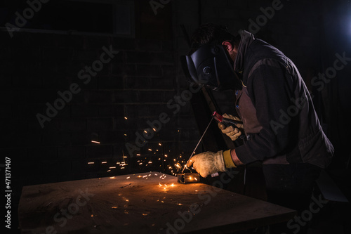 Welder using an electrode to weld a metal plate with yellow sparks