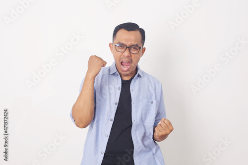 Happy energetic young Asian man yelling and clenching fists isolated on white studio background