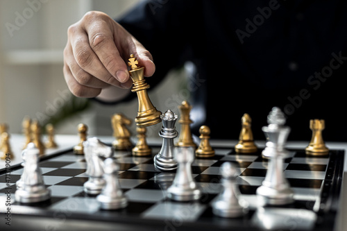 Person playing chess board game, business man concept image holding chess pieces like business competition and risk management, planning business strategies to defeat business competitors.