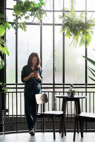 Hard work and Relax time. Asian businesswoman hard on laptop at her desk. Woman using smartphone apps, send message, play mobile games while standing near the window in relax time.