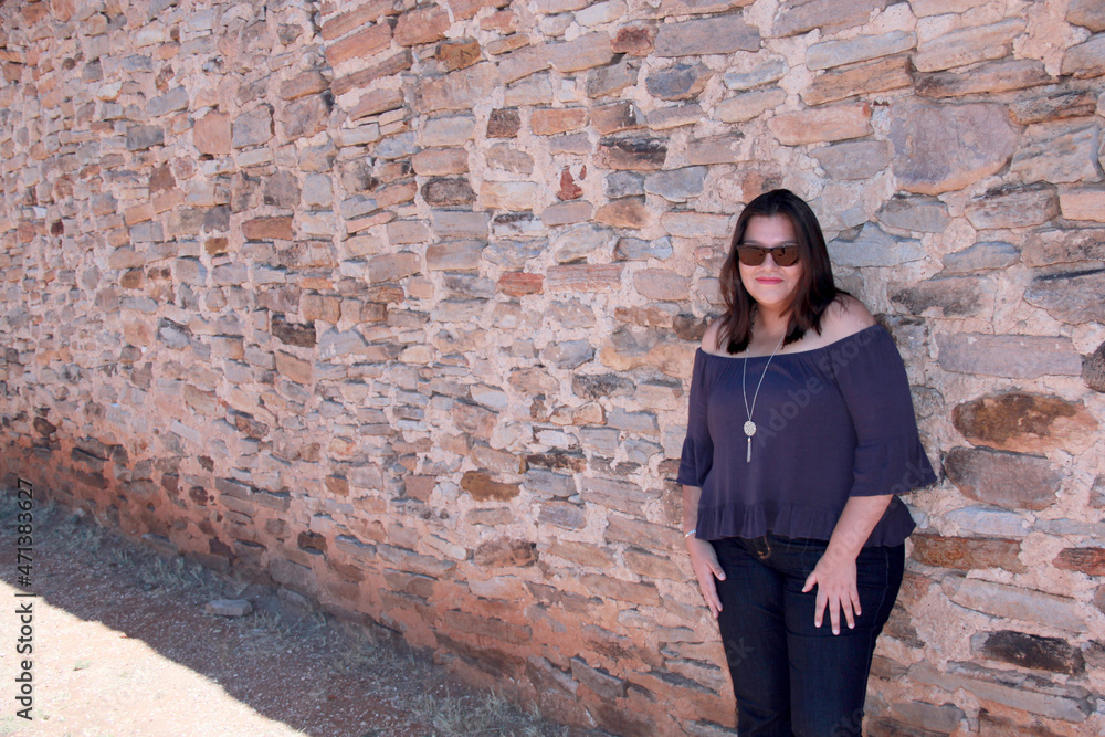 Latin adult woman with sunglasses and stone wall background relaxed and happy enjoying the sunny day
