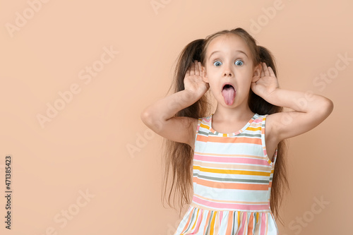 Fototapeta Portrait of little girl showing tongue on beige background