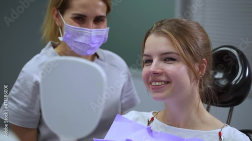 Orthodontist with patient at appointment. Pretty blonde woman tries on aligners looking in mirror spbas and smiles while doctor sits nearby in clinic closeup photo