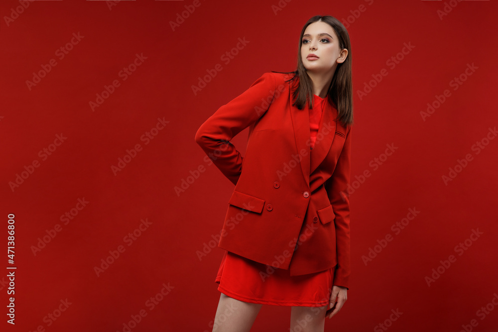 High fashion photo of elegant young model in red suit, jacket, short skirt, socks. Beautiful young woman, slim figure. Studio shot. Red background. Monochrome color High fashion photo of elegant young model in red suit, jacket, short skirt, socks. Beautiful young woman, slim figure. Studio shot. Red background. Monochrome color