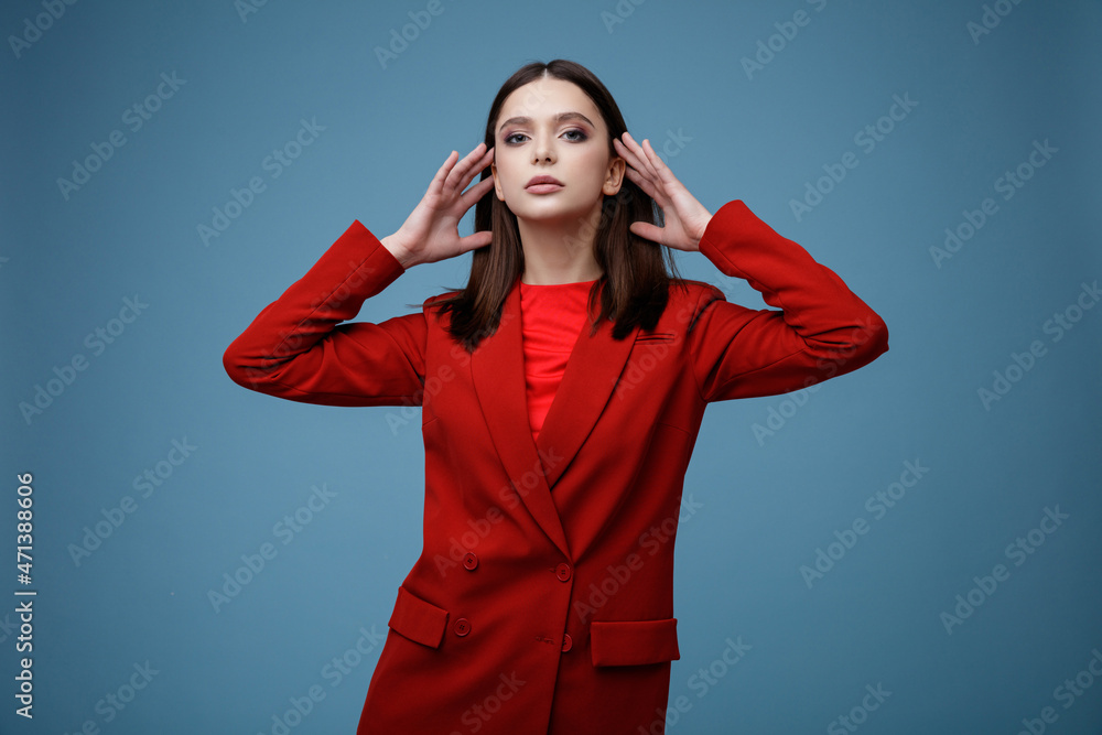 High fashion photo of elegant young model in red suit, jacket, short skirt, socks. Beautiful young woman, slim figure. Studio shot. Blue background. High fashion photo of elegant young model in red suit, jacket, short skirt, socks. Beautiful young woman, slim figure. Studio shot. Blue background.