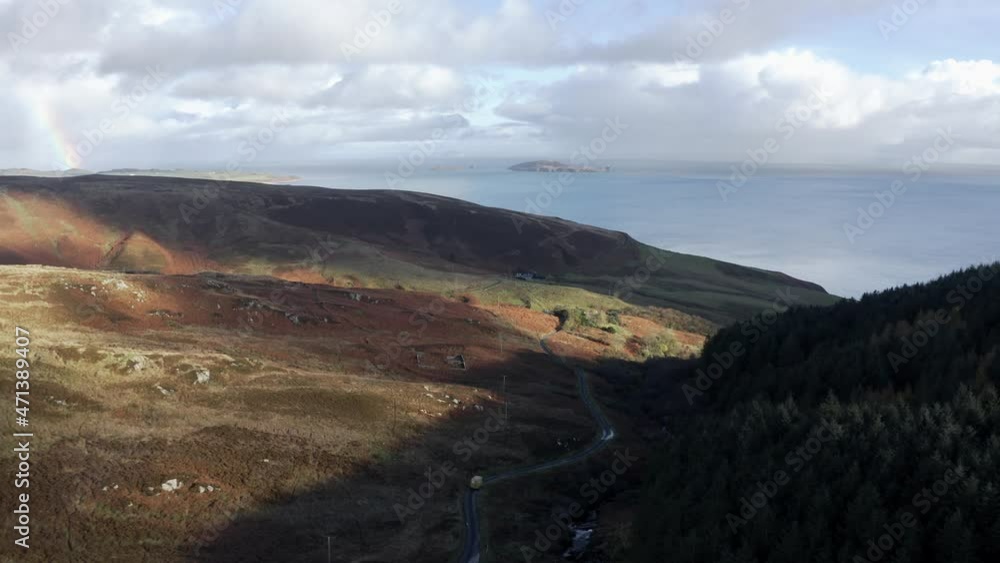 Flying over a road with passing cars between a wooded hill and the plains of the Scottish Highlands called Mull of Kintyre Flying over a road with passing cars between a wooded hill and the plains of the Scottish Highlands called Mull of Kintyre