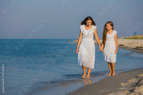 mom and daughter in white dresses walk on the beach