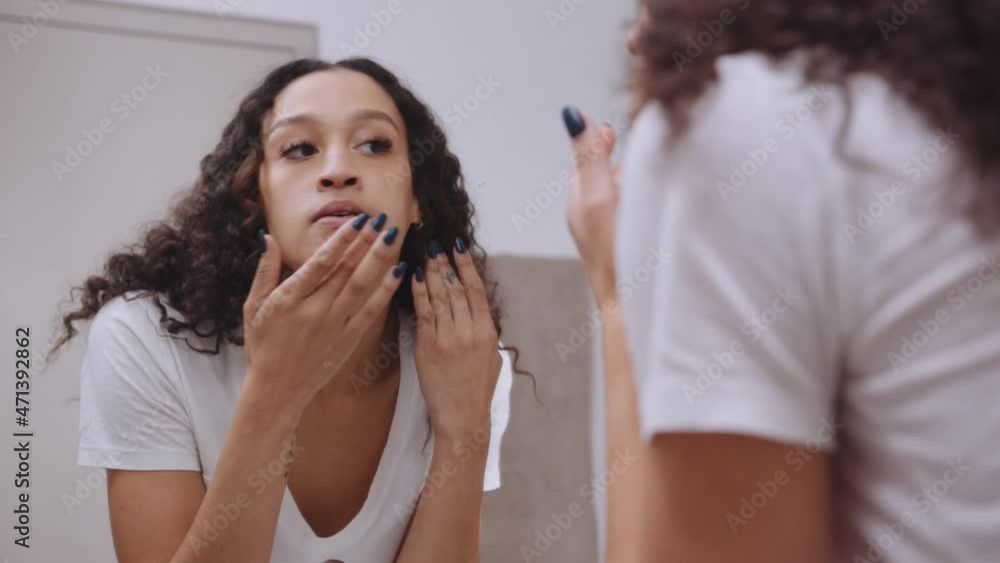 Multi-cultural young female looking for blemishes on her face in modern bathroom mirror Multi-cultural young female looking for blemishes on her face in modern bathroom mirror