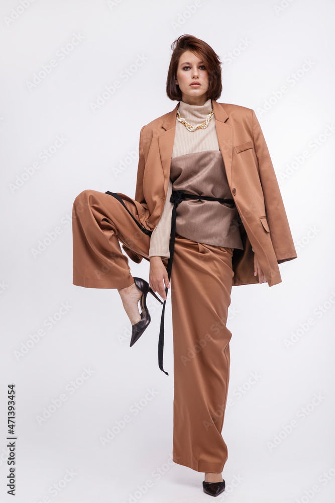 Fashion photo of a beautiful elegant young woman in a pretty oversize brown and beige suit, corset, jacket, pants posing over white background. Bob haircut. Studio Shot. Portrait Fashion photo of a beautiful elegant young woman in a pretty oversize brown and beige suit, corset, jacket, pants posing over white background. Bob haircut. Studio Shot. Portrait