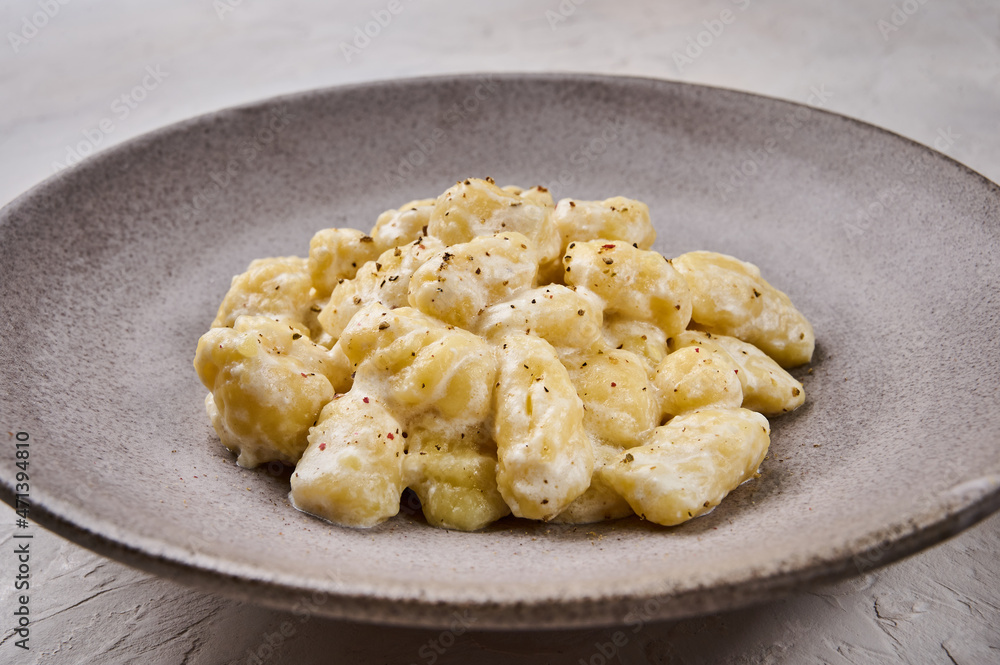 Close up homemade gnocchi, prepared with potato and whole grain flour dough with cream sauce and pepper on gray plate, selective focus Close up homemade gnocchi, prepared with potato and whole grain flour dough with cream sauce and pepper on gray plate, selective focus