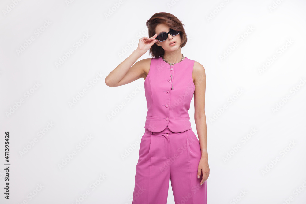 Fashion photo of a beautiful elegant young woman in a pretty pink suit, black boots, stylish sunglasses posing over white background. Bob haircut. Studio Shot. White and pink colors Fashion photo of a beautiful elegant young woman in a pretty pink suit, black boots, stylish sunglasses posing over white background. Bob haircut. Studio Shot. White and pink colors
