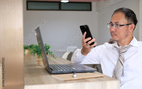 Concept of unrecognisable businessman using a laptop while working remotely, hands working on modern laptop. Office desktop and using smartphone 