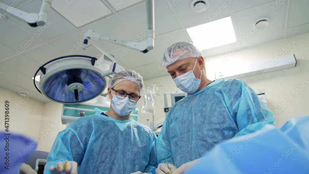 Group of doctors performing operation to a patient. Surgeons in medical uniform and masks working in the operating room. Neurosurgery concept Group of doctors performing operation to a patient. Surgeons in medical uniform and masks working in the operating room. Neurosurgery concept