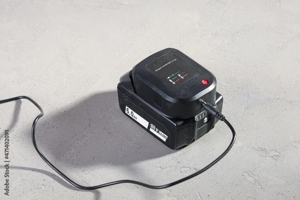 Powerful battery for electrical tool with connected charger on concrete gray surface close-up Powerful battery for electrical tool with connected charger on concrete gray surface close-up