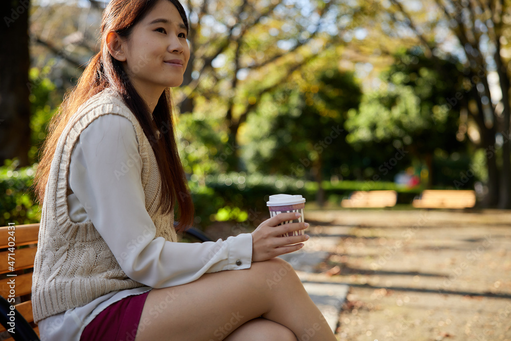 コーヒーカップを持ってベンチに座っているアジア人女性 コーヒーカップを持ってベンチに座っているアジア人女性
