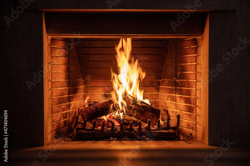 Fireplace burning firewood, fire flames on wood logs, bricks background. Cozy warm home at Christmas