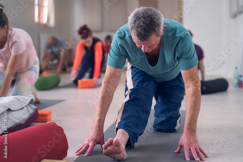 Older adult male, stretching his legs, during a group yoga class.