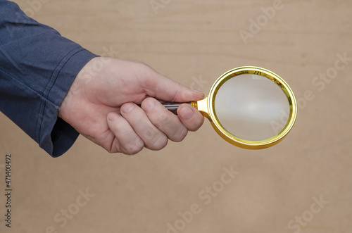 An adult man holds a magnifying glass in his hand against a brow