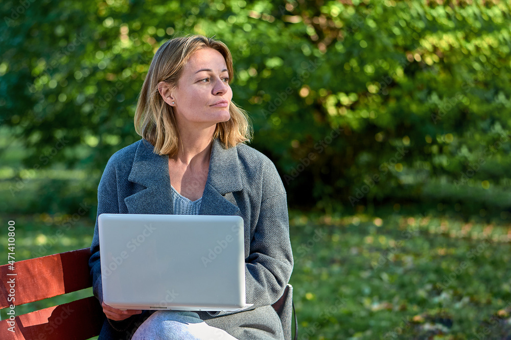 A woman with a laptop is sitting on a park bench on a sunny summer day A woman with a laptop is sitting on a park bench on a sunny summer day