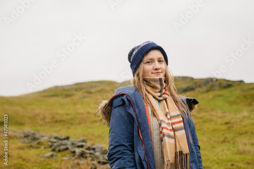 Young beautiful woman in blue coat, hat and scarf in autumn rainy and cloudy weather. Field in background.