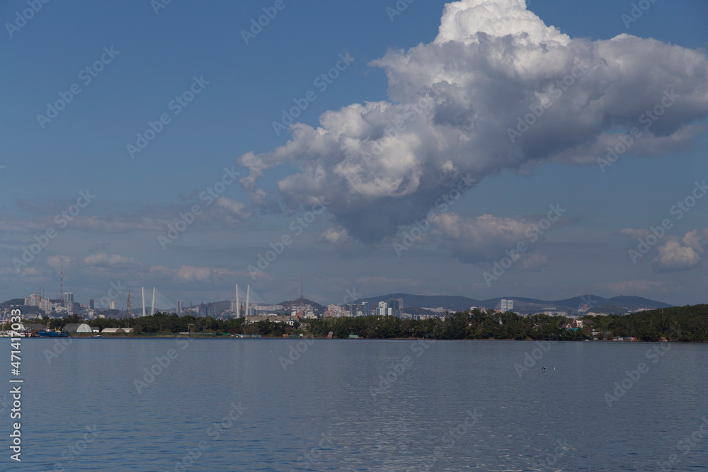 day view of the sea, islets, capes, white clouds and blue sky and the city on the hills in the background. Shot in the Novik harbor on island Russky in Vladivostok, Russia