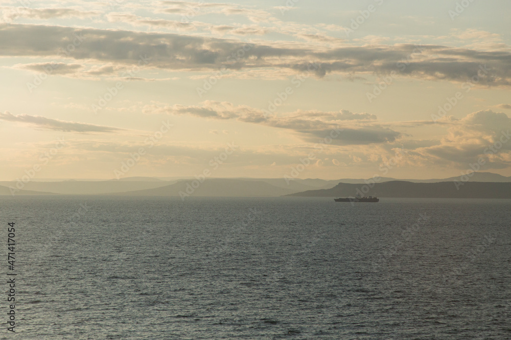 sunset dusk seascape view of a lonely boat on calm water, with beautiful clouds, islands and islets on a soft yellow sky and white clouds background. Vladivostok, Russia sunset dusk seascape view of a lonely boat on calm water, with beautiful clouds, islands and islets on a soft yellow sky and white clouds background. Vladivostok, Russia